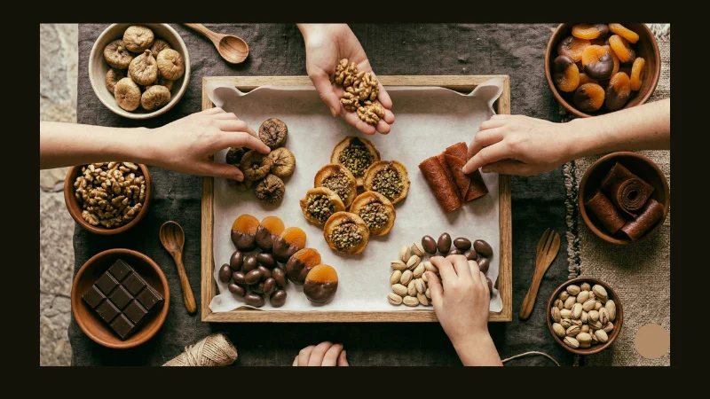  Overhead flat lay of hands arranging figs, walnuts, apricots and bastegh rolls into a wooden tray lined with parchment paper. how to make dry fruit basket at home armenian dried fruits wooden tray assembly..