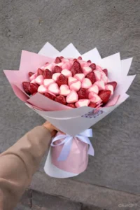 Hand-held edible bouquet made of fresh strawberries and heart-shaped marshmallows wrapped in pastel pink paper with a white ribbon  