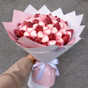 Hand-held edible bouquet made of fresh strawberries and heart-shaped marshmallows wrapped in pastel pink paper with a white ribbon