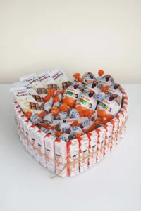 A 25cm heart-shaped gift box filled with Kinder chocolate bars and Kinder Surprise eggs, tied with rustic twine, presented on a white surface.