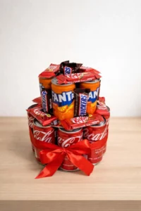 Two-tier novelty gift tower built from Coca-Cola and Fanta cans, decorated with Snickers and KitKat bars, tied with a red satin ribbon 