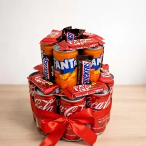 Two-tier novelty gift tower built from Coca-Cola and Fanta cans, decorated with Snickers and KitKat bars, tied with a red satin ribbon