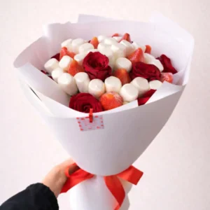 Hand-held edible bouquet featuring fresh red roses, juicy strawberries, and white marshmallows wrapped in white paper with a red ribbon