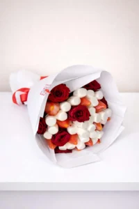 Hand-held edible bouquet featuring fresh red roses, juicy strawberries, and white marshmallows wrapped in white paper with a red ribbon ready to get delivered for free to abovyan and yerevan 