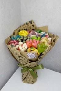 Hand-held edible bouquet made of colorful gummy and jelly candies wrapped in heart-printed kraft paper with a green ribbon 