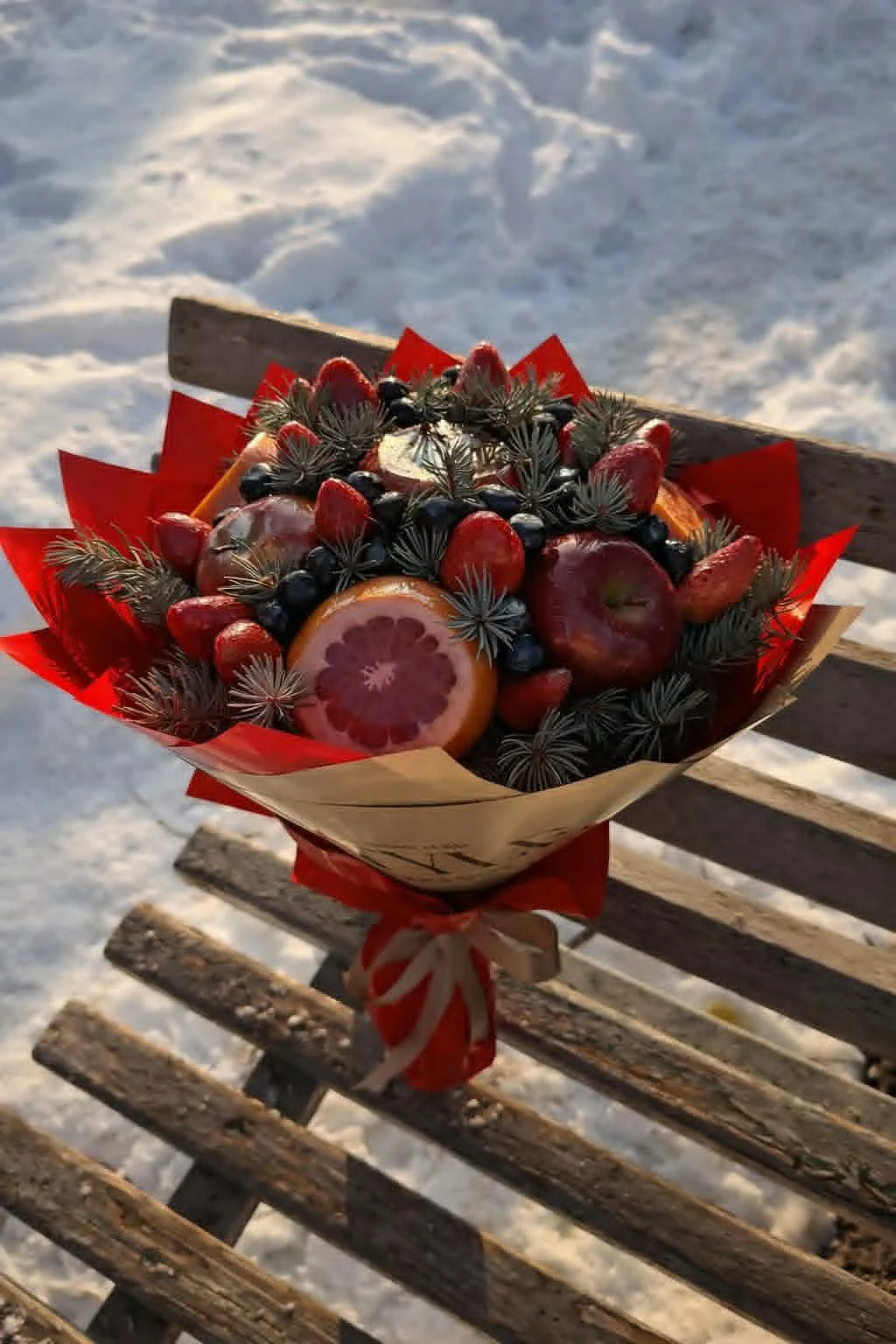 Rustic edible bouquet made of fresh strawberries, sliced grapefruit, red apples, and pine branches wrapped in brown kraft paper
