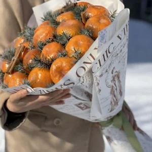 Rustic winter edible bouquet made of fresh tangerines, pine branches, and cinnamon sticks wrapped in vintage newspaper-print brown kraft paper