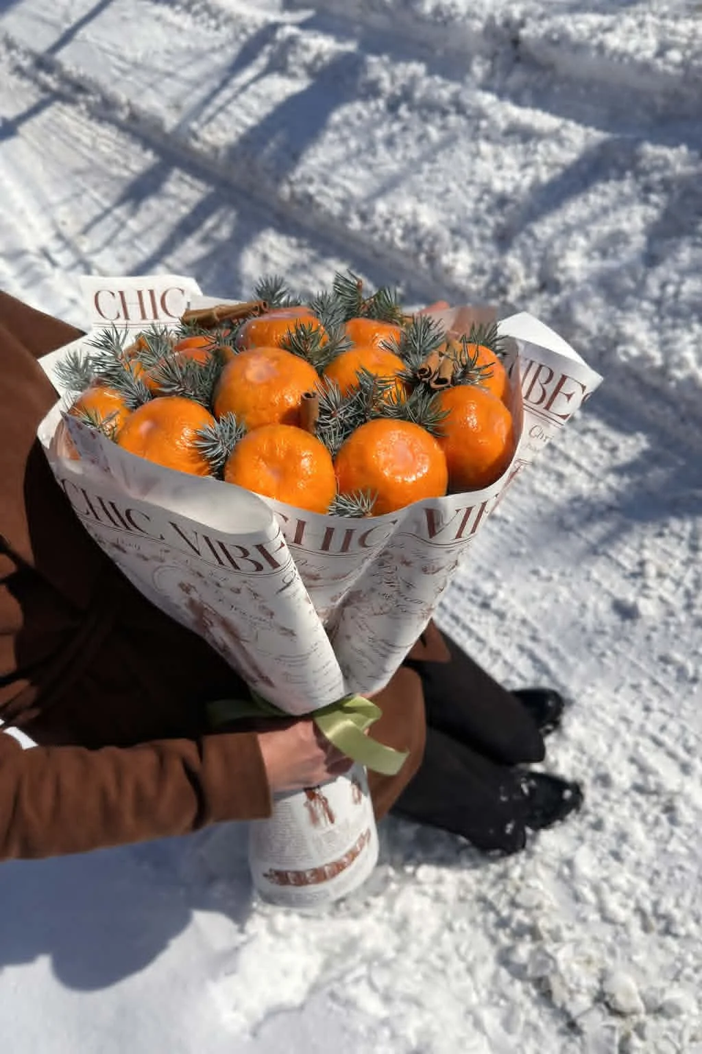 Rustic winter edible bouquet made of fresh tangerines, pine branches, and cinnamon sticks wrapped in vintage newspaper-print brown kraft paper