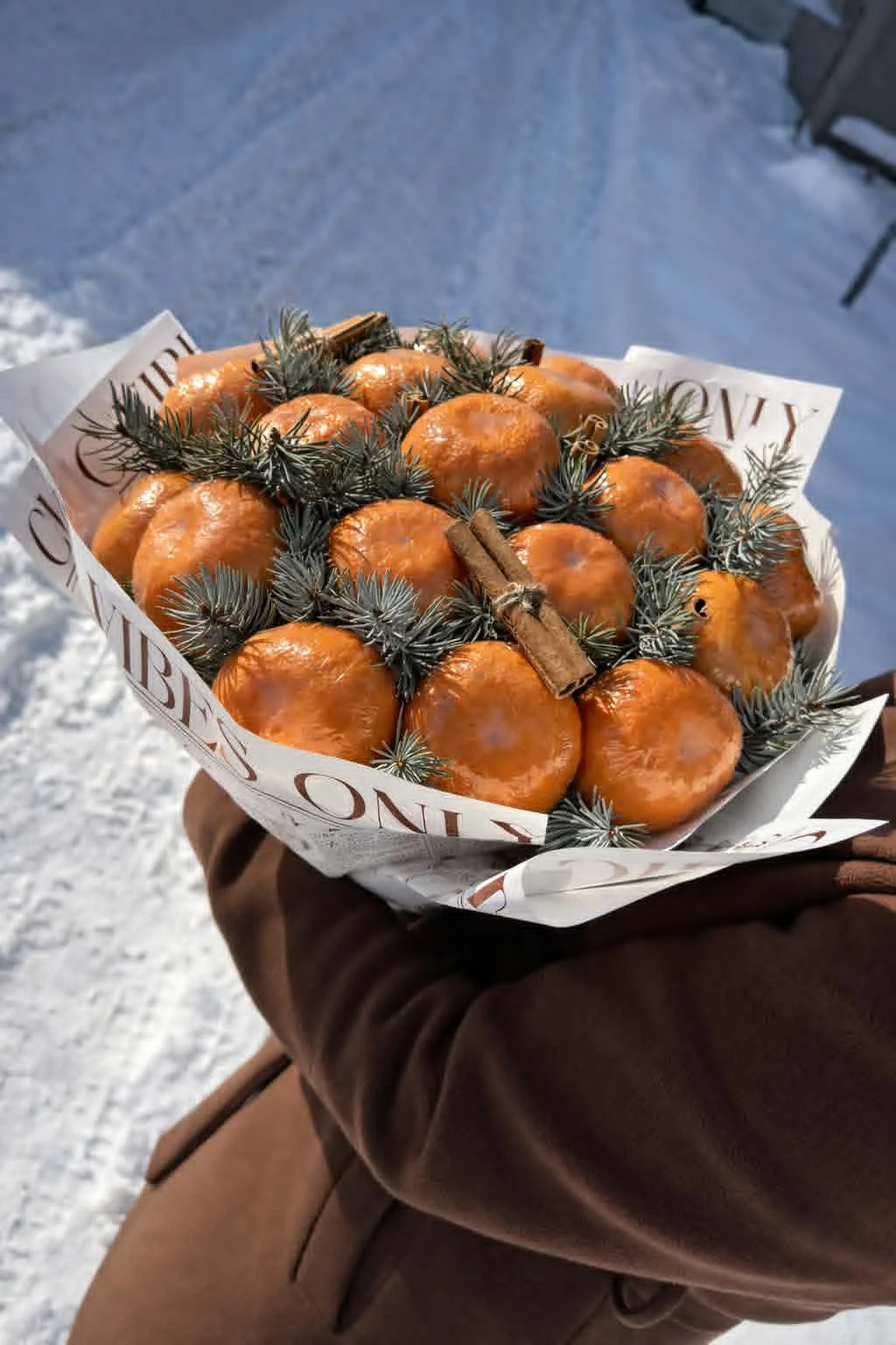 Rustic winter edible bouquet made of fresh tangerines, pine branches, and cinnamon sticks wrapped in vintage newspaper-print brown kraft paper