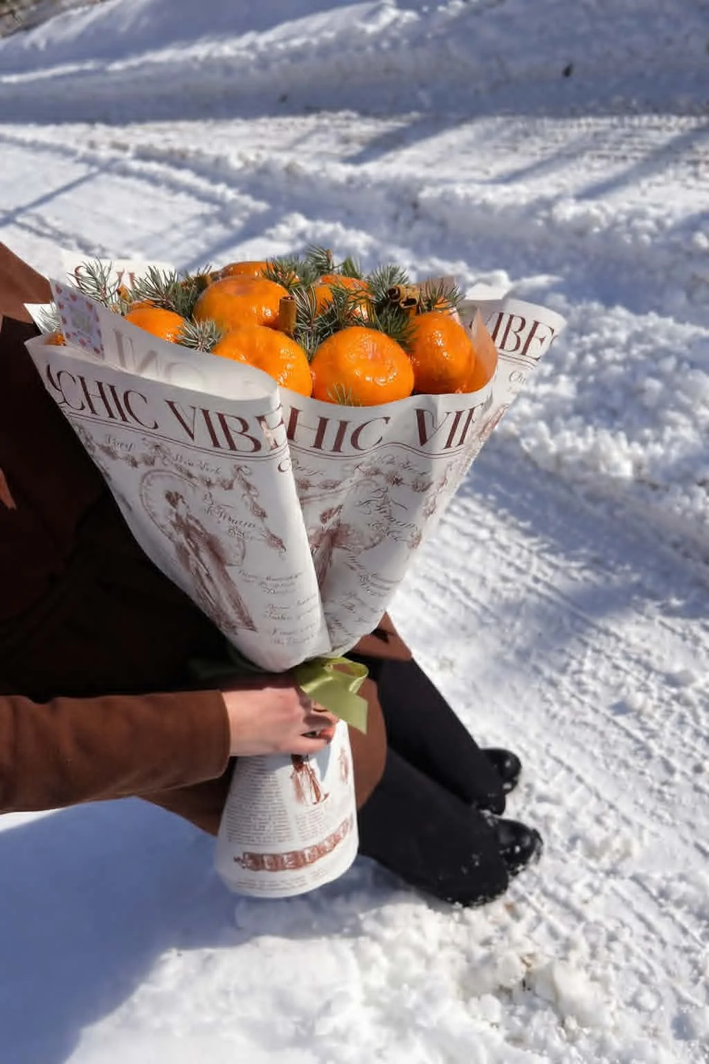 Rustic winter edible bouquet made of fresh tangerines, pine branches, and cinnamon sticks wrapped in vintage newspaper-print brown kraft paper