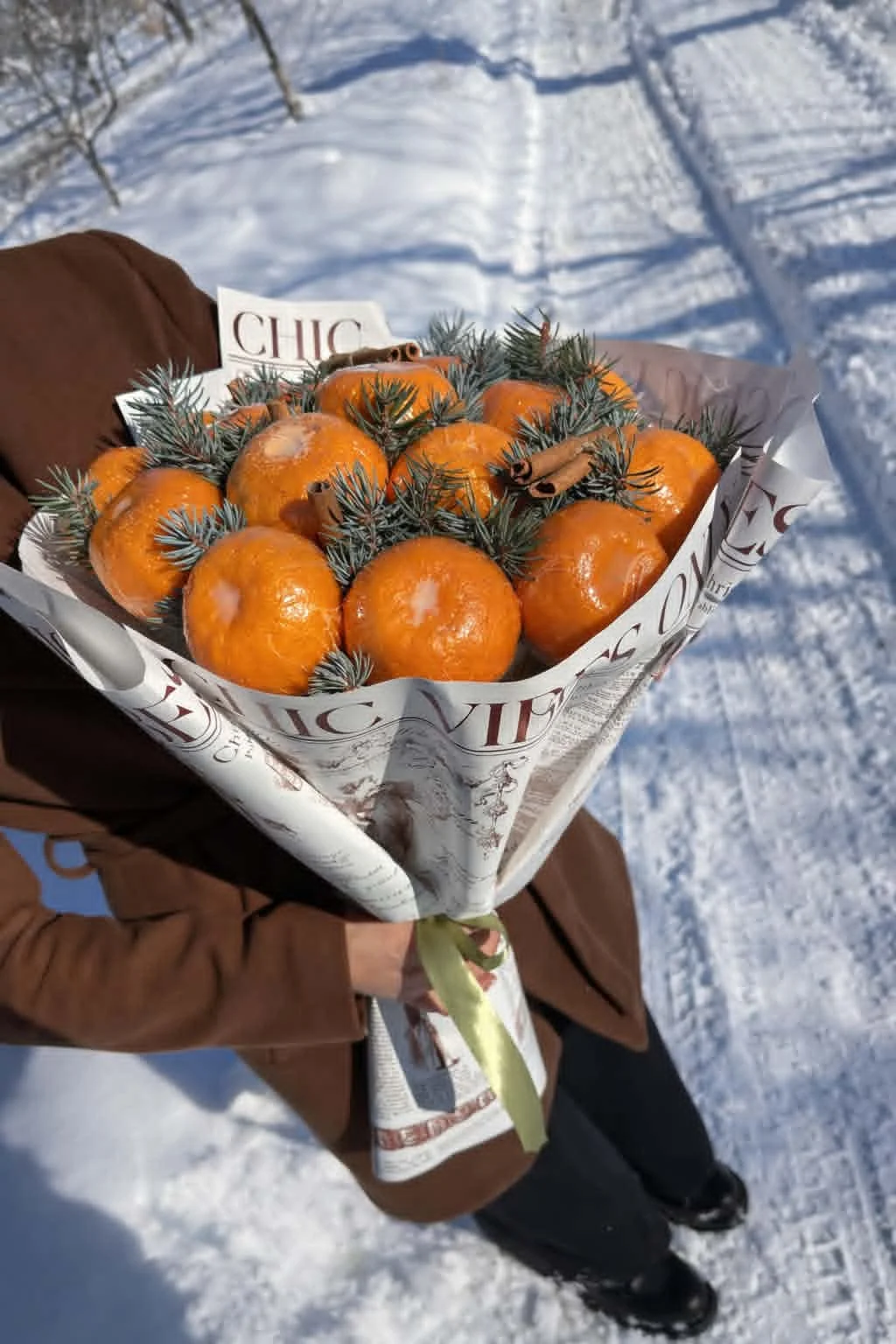 Rustic winter edible bouquet made of fresh tangerines, pine branches, and cinnamon sticks wrapped in vintage newspaper-print brown kraft paper