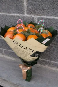 Rustic winter edible bouquet made of fresh tangerines, pine branches, and candy canes wrapped in printed brown kraft paper  