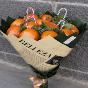 Rustic winter edible bouquet made of fresh tangerines, pine branches, and candy canes wrapped in printed brown kraft paper