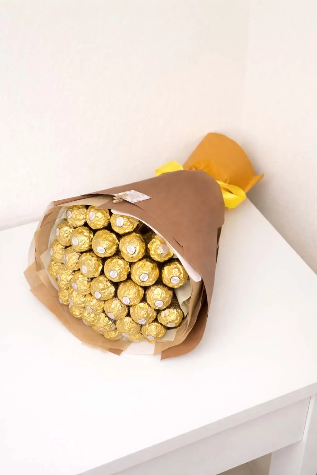 Premium bouquet made entirely of gold-wrapped Ferrero Rocher chocolates, styled in brown kraft paper with a bright yellow ribbon