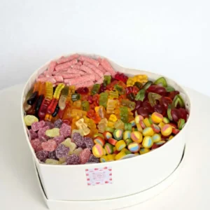 White heart-shaped gift box filled with a colorful assortment of jelly candies, sour sticks, and gummy bears