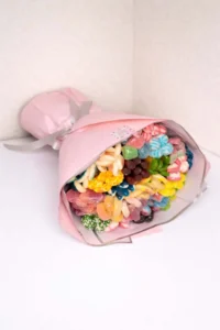 Large hand-held edible bouquet made of colorful gummy and jelly candies wrapped in pastel pink paper with a gray ribbon