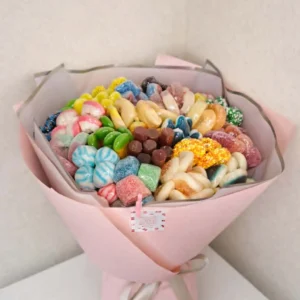 Large hand-held edible bouquet made of colorful gummy and jelly candies wrapped in pastel pink paper with a gray ribbon
