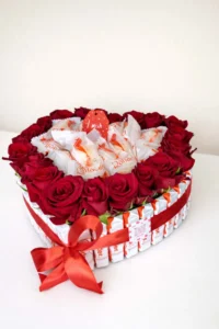 Large heart-shaped gift arrangement framed by Kinder chocolate bars, filled with fresh red roses and Raffaello candies, tied with a red ribbon  