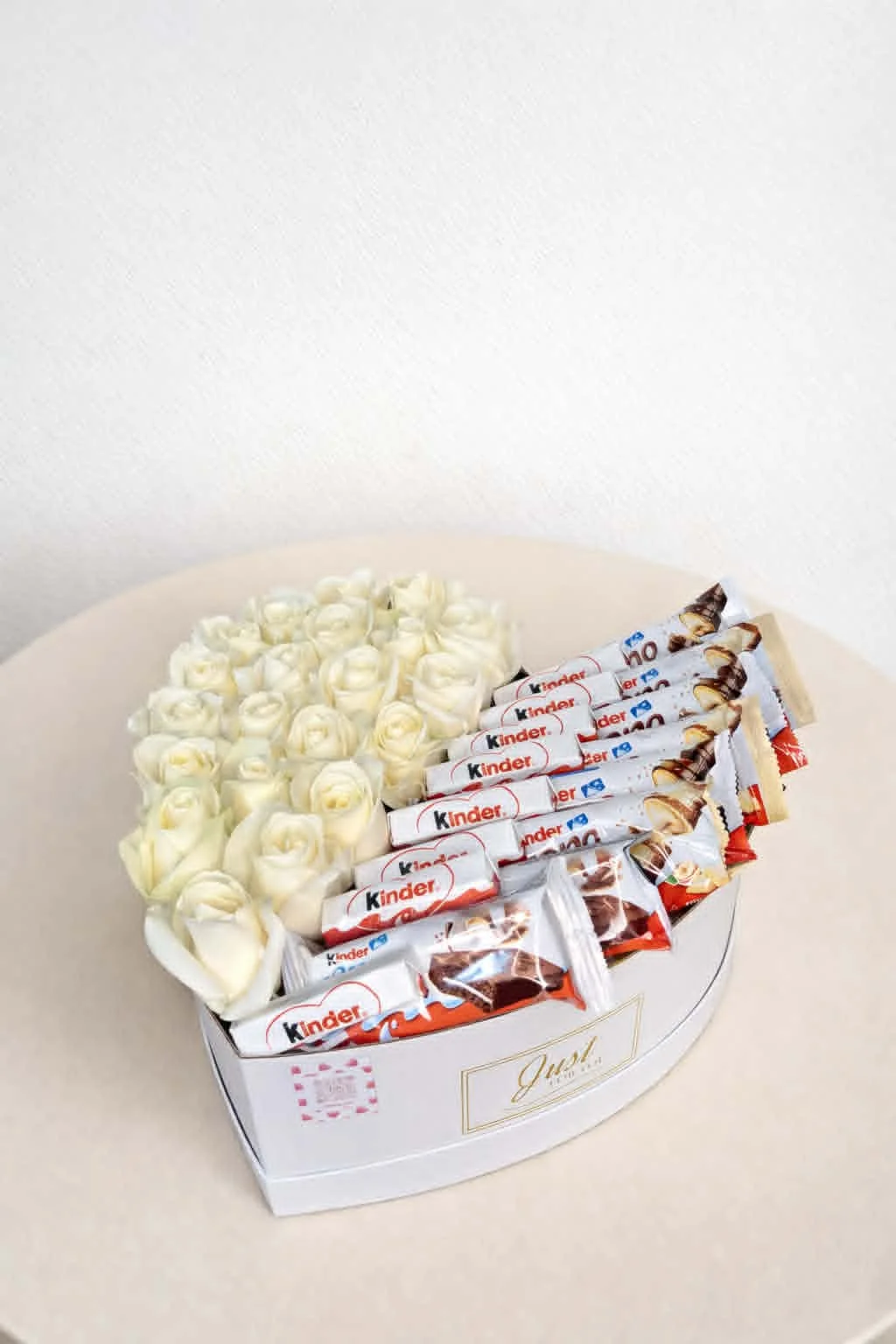 Large white heart-shaped gift box, half-filled with fresh white roses and half-filled with Kinder chocolate bars