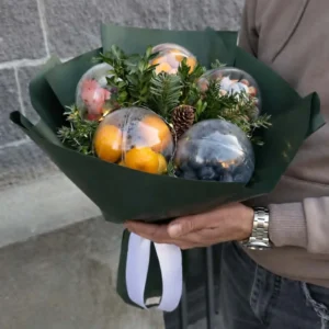 Premium winter edible gifts arrangement in a handheld bouquet of tangerines, nuts, and evergreen boughs in dark green paper wrapping.