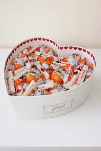 Large 40cm white heart-shaped hat box overflowing with assorted Kinder chocolates: Kinder Surprise, Bueno, bars, Schoko-Bons, adorned with red hearts