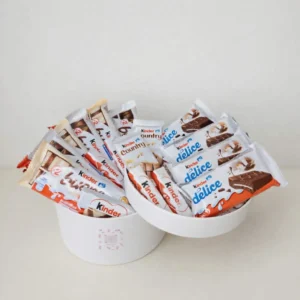 A sleek white round gift box overflowing with a variety of Kinder Bueno, Kinder Delice, and Kinder Country chocolate bars.