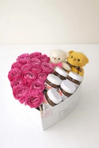 Luxury white heart-shaped gift box filled with fresh magenta peony roses, Nutella chocolate jars, and two teddy bears  